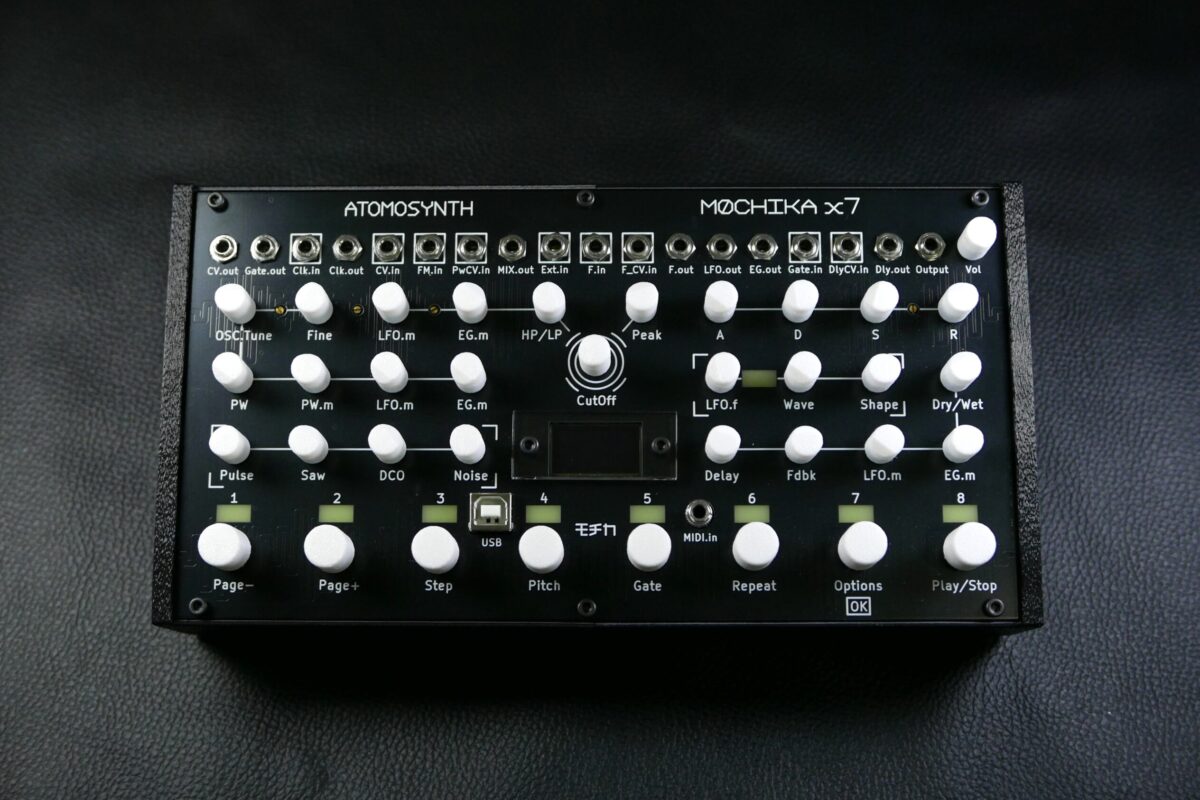 AtomoSynth Mochika X7 en version bureau vu de dessus : façade noire, boutons blancs, rangée de jacks, écran OLED et huit touches de pas